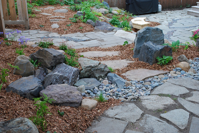 A lush landscaped garden featuring colorful rocks strategically placed among vibrant foliage and natural stone pathway, enhancing outdoor aesthetics